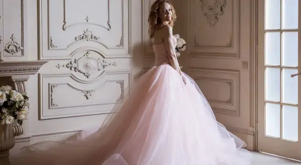 Kobieta w różowej sukni księżniczki z bukietem kwiatów w eleganckim wnętrzu.