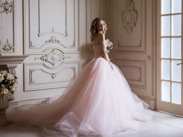 Kobieta w różowej sukni księżniczki z bukietem kwiatów w eleganckim wnętrzu.
